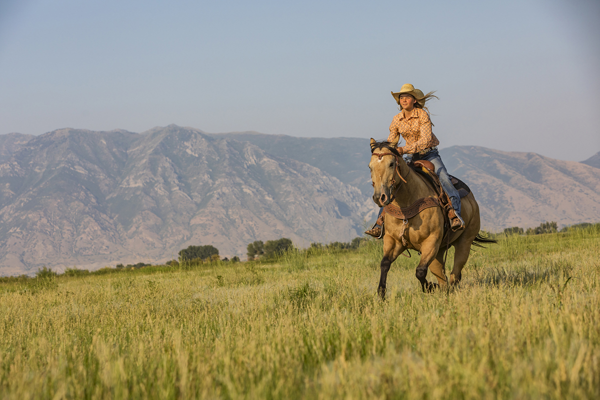 Young woman riding a horse across the prairie with mountains in the background